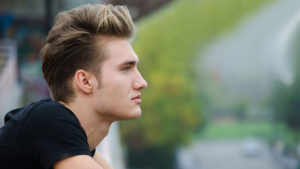 Profile shot of attractive blond young man in city, looking afar outdoors